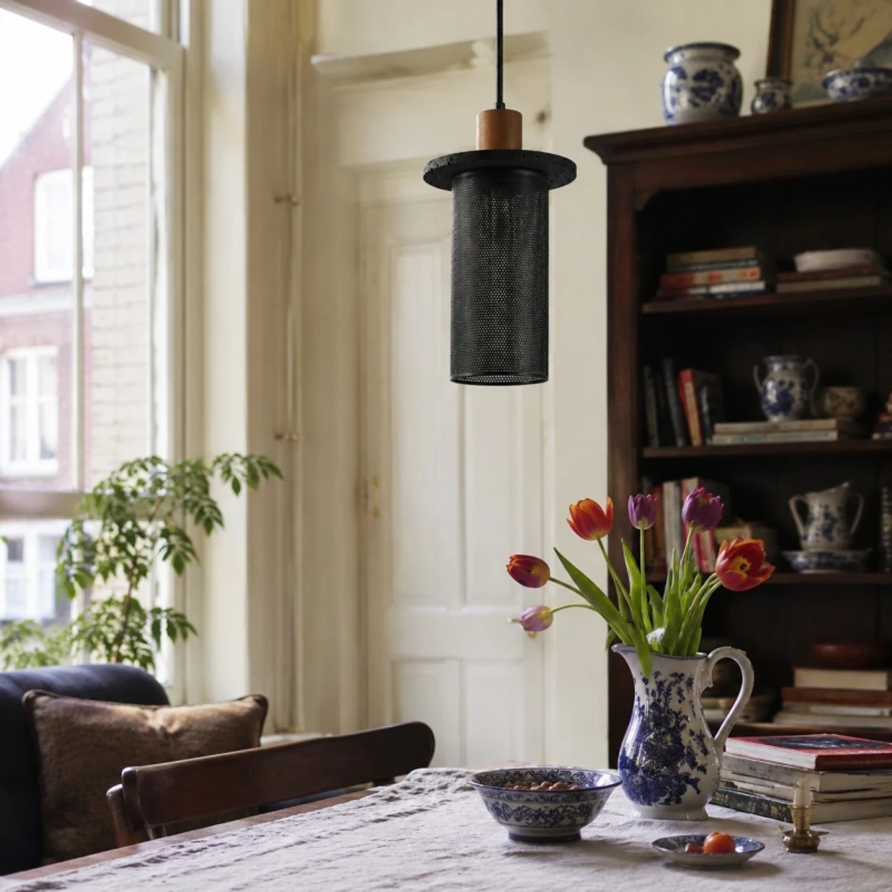 Black woven mesh pendant light above a window-side dining table